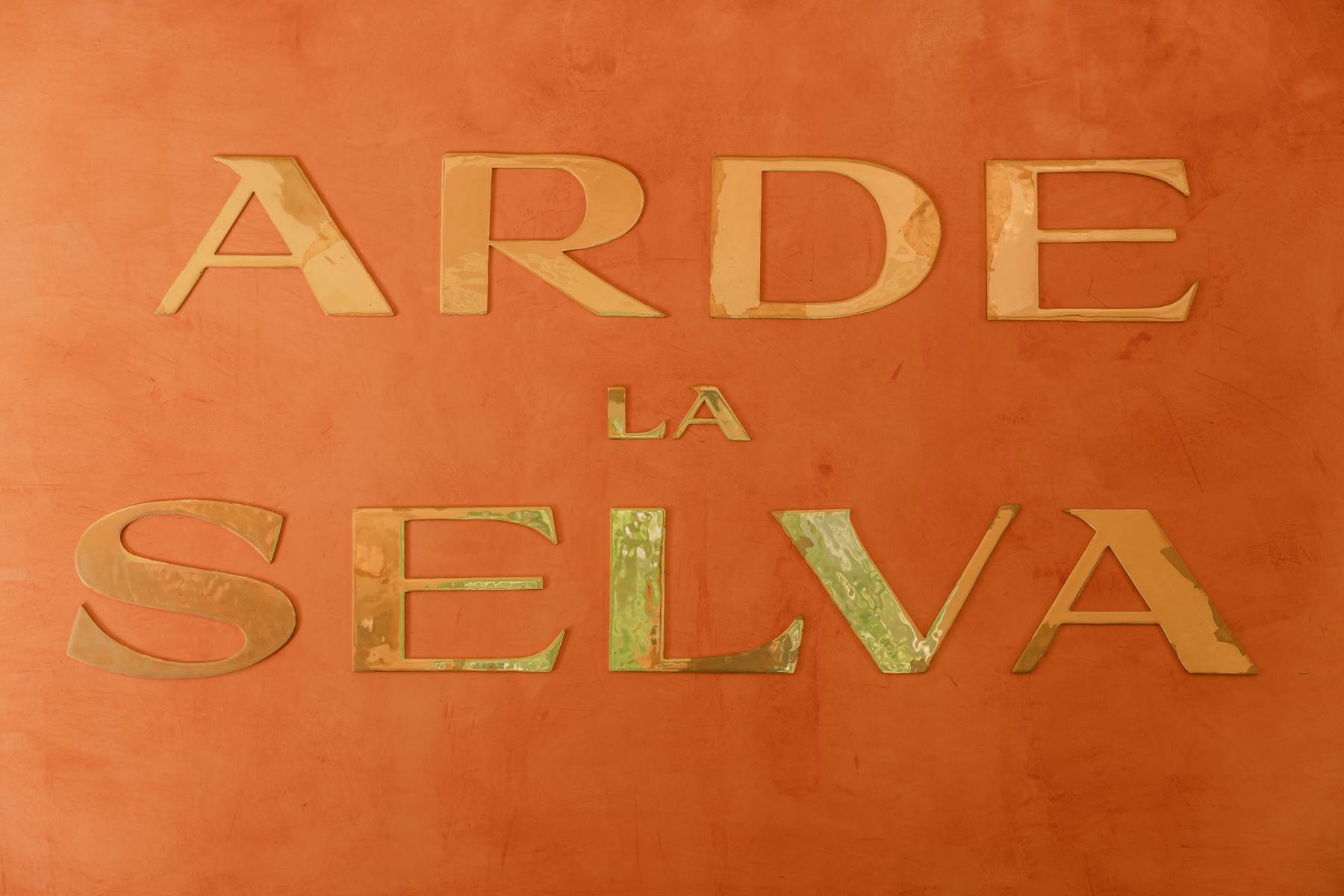 Las letras doradas de Arde La Selva sobre el muro naranja